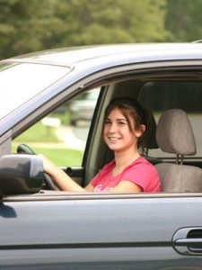 A young female in the driver side of a car representing a teen driver