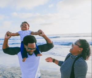 Family of 3 on the beach with child on shoulders