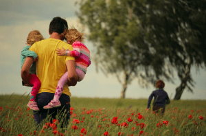 Father carrying two children through open field with flowers